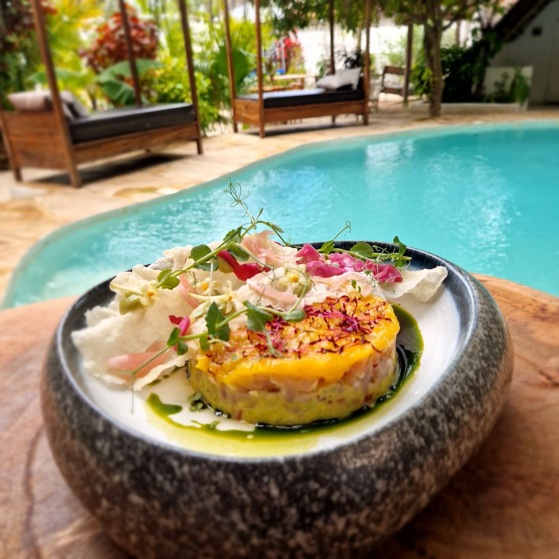 A plated dish in a stone bowl with the pool and daybeds behind it