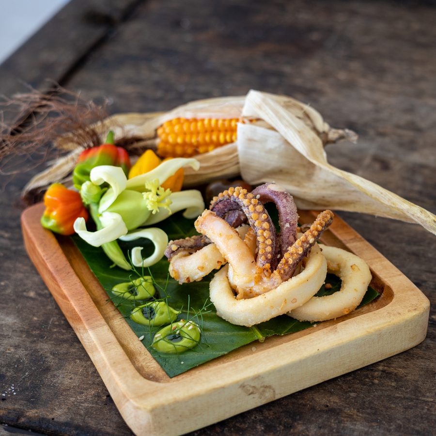 Calamari on a wooden board with green sauce and carved vegetables