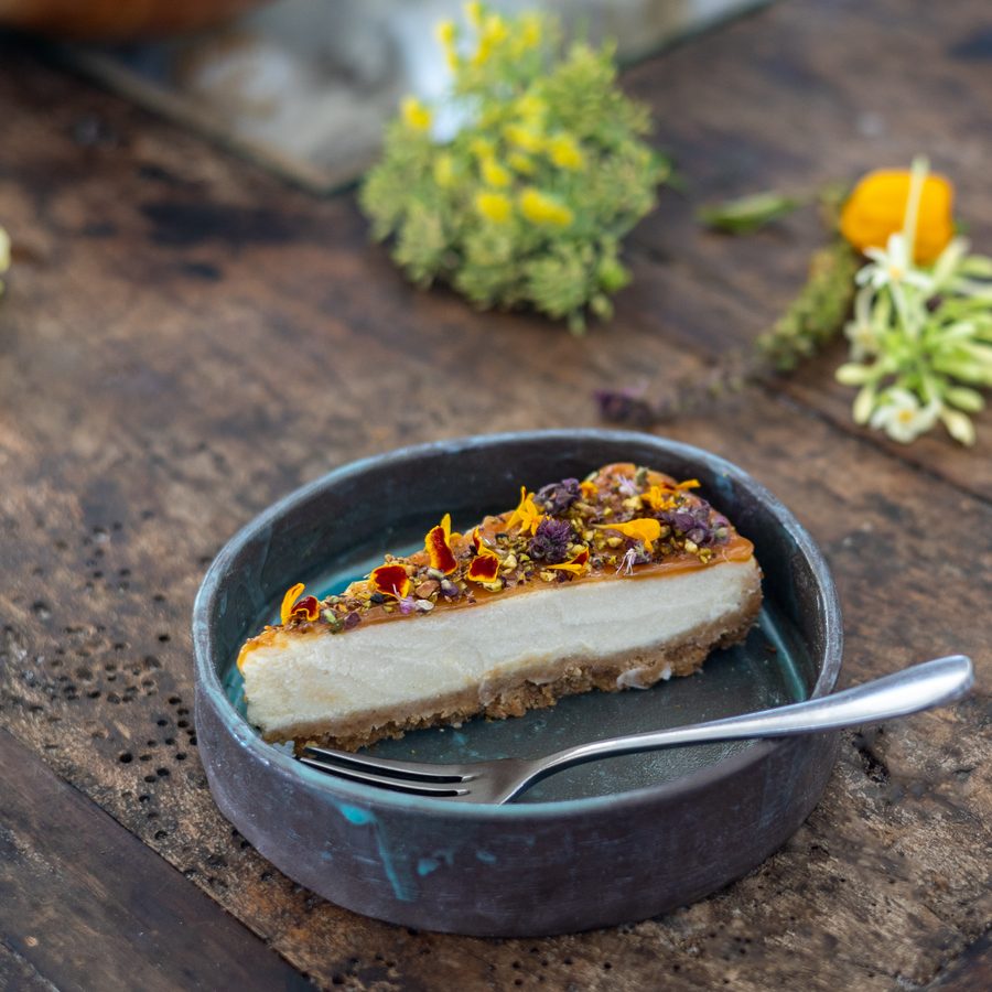 A slice of cheesecake with a caramel and nut topping in a blue dish