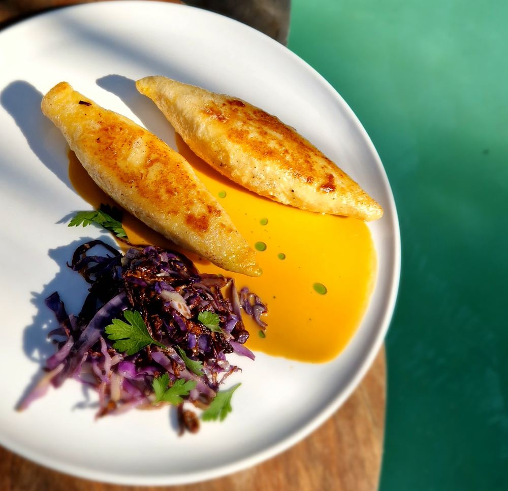 Two golden pastries with red cabbage slaw and a yellow sauce