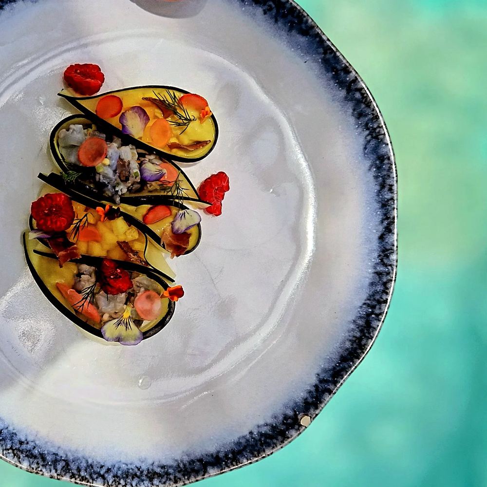 Filled shells with edible flowers on a blue-rimmed plate, held over the pool