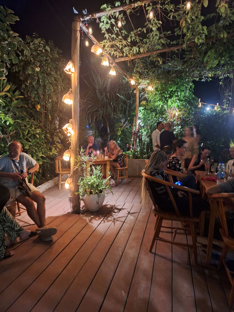 Guests at tables on the deck at night under strings of lanterns