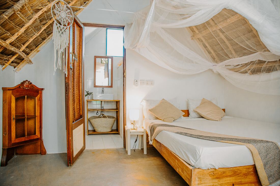 Bungalow room under a thatched roof with a mosquito net over the bed
